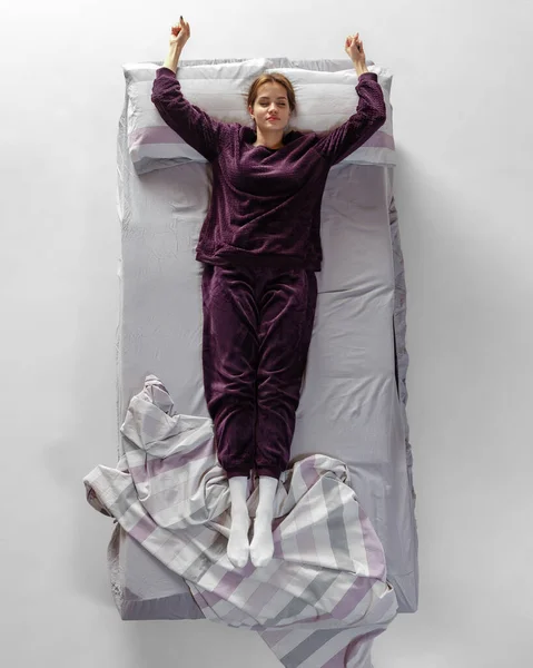 Retrato creativo de una joven con ropa de casa de color vino, pijamas durmiendo en una cama grande. Concepto de salud, interior del hogar, tiempo de relax, familia, sueños —  Fotos de Stock