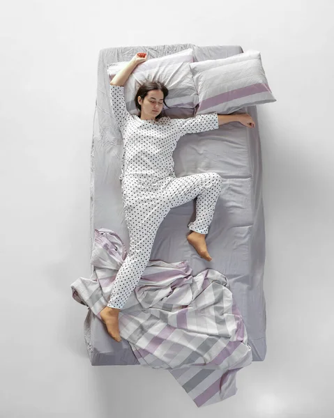 Beyaz pijamalı uyuyan genç bir kız büyük gri bir yatakta yatıyor. Sağlık kavramı, ev içi, dinlenme zamanı, aile, hayaller