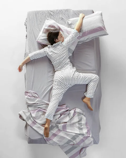 Vista aérea joven durmiendo chica en pijama blanco acostado en gran cama gris. Concepto de salud, interior del hogar, tiempo de relax, familia, sueños —  Fotos de Stock