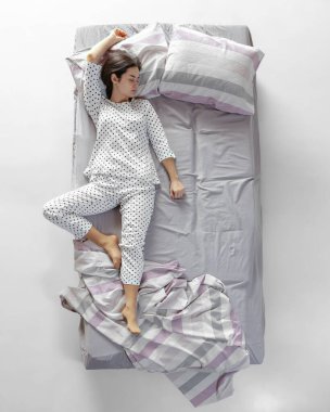 Beyaz pijamalı uyuyan genç bir kız büyük gri bir yatakta yatıyor. Sağlık kavramı, ev içi, dinlenme zamanı, aile, hayaller