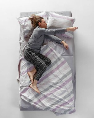 Gri renkli ev kıyafetleri giyen genç adam, büyük yatakta uyuyan pijamalar. Sağlık kavramı, ev içi, dinlenme zamanı, aile, hayaller. Üst görünüm