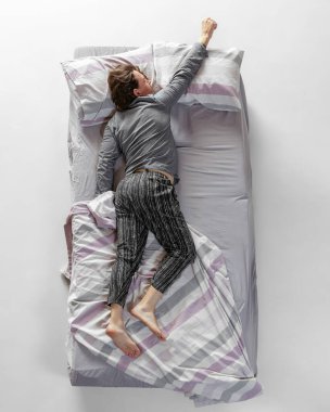 Gri renkli ev kıyafetleri giyen genç adam, büyük yatakta uyuyan pijamalar. Sağlık kavramı, ev içi, dinlenme zamanı, aile, hayaller. Üst görünüm