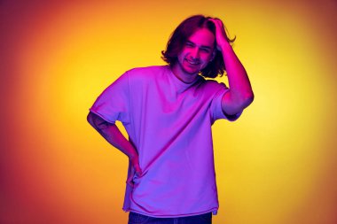 Genç duygusal adamın stüdyo fotoğrafı, öğrenci mor neon ışıkta turuncu arka planda izole edilmiş poz veriyor. Duygular, güzellik, moda kavramı