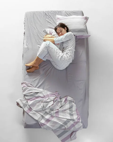 Vista aérea joven durmiendo chica en pijama blanco acostado en gran cama gris. Concepto de salud, interior del hogar, tiempo de relax, familia, sueños —  Fotos de Stock