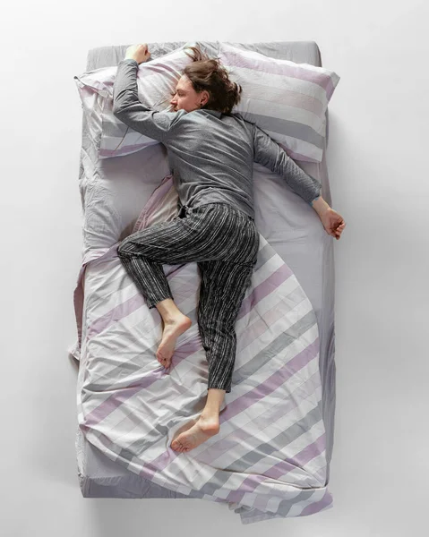 Gri renkli ev kıyafetleri giyen genç adam, büyük yatakta uyuyan pijamalar. Sağlık kavramı, ev içi, dinlenme zamanı, aile, hayaller. Üst görünüm — Stok fotoğraf
