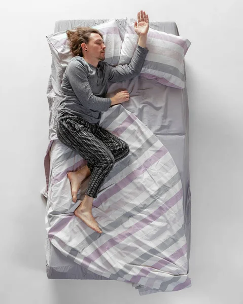 Młody człowiek w szarym kolorze, w piżamie śpiący w dużym łóżku. Koncepcja zdrowia, wnętrze domu, czas relaksu, rodzina, marzenia. Widok z góry — Zdjęcie stockowe