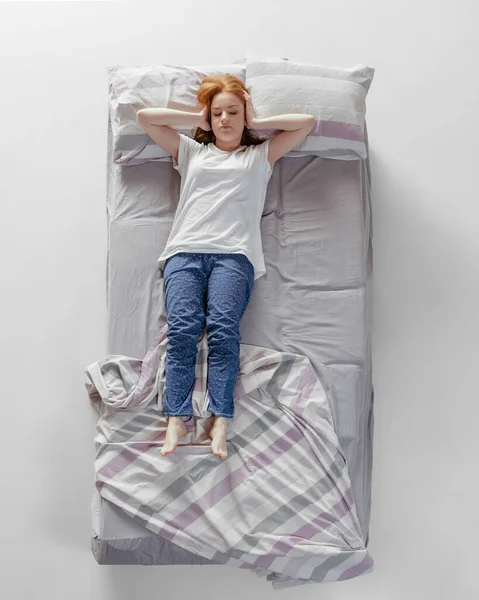 Luftaufnahme eines rothaarigen jungen schlafenden Mädchens in Baumwollhosen, das in einem riesigen grauen Bett liegt. Konzept der Gesundheit, Wohnkultur, Entspannungszeit, Familie, Träume — Stockfoto
