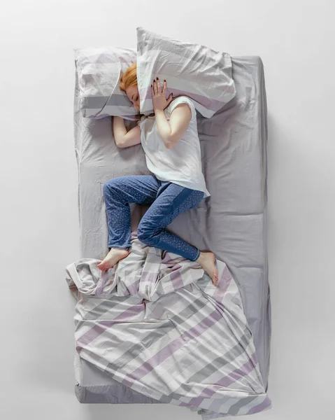 Vue aérienne de jeune fille rousse endormie dans des vêtements de maison en coton couché dans un énorme lit gris. Concept de santé, intérieur de la maison, temps de détente, famille, rêves — Photo