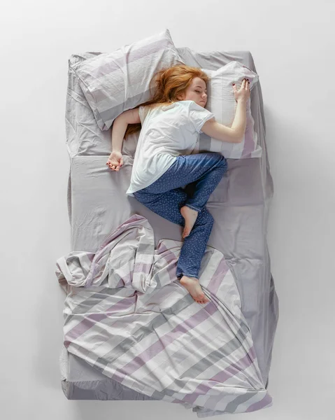 Vue aérienne de jeune fille rousse endormie dans des vêtements de maison en coton couché dans un énorme lit gris. Concept de santé, intérieur de la maison, temps de détente, famille, rêves — Photo