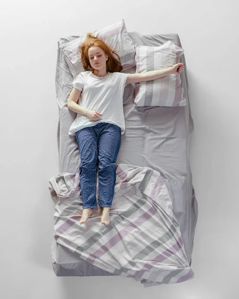 Vista aérea de la joven pelirroja dormida en ropa de casa de algodón acostada en una enorme cama gris. Concepto de salud, interior del hogar, tiempo de relax, familia, sueños — Foto de Stock