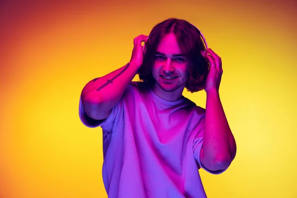 Retrato de medio cuerpo del joven guapo en ropa casual de estilo juvenil aislada sobre fondo naranja en luz de neón, filtro. Concepto de emociones, belleza, moda —  Fotos de Stock