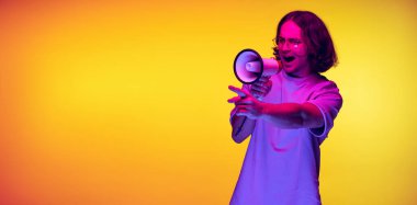 Beyaz tişörtlü genç bir adam megafona bağırıyor turuncu arka planda neon ışıkta izole edilmiş. Duygular, moda, gençlik kavramı