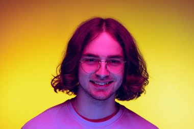 Genç bir adamın portresi, günlük giysiler içindeki öğrenci turuncu arka planda mor neon ışıkta izole edilmiş. Duygular, güzellik, moda kavramı