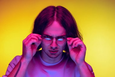 Yakından genç bir adam, günlük giysiler içinde gözlük takan mor ışıklı turuncu arka planda izole edilmiş gözlük takan bir öğrenci. Duygular, güzellik, moda kavramı