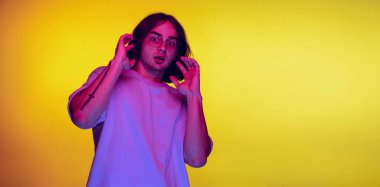 Stüdyoda korkmuş genç bir adamın fotoğrafı. Mor neon ışıkta turuncu arka planda poz veren bir öğrenci. Duygular, güzellik, moda kavramı