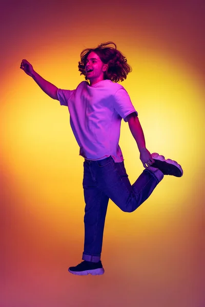 Full-length portret van jonge opgewonden man springen geïsoleerd op oranje achtergrond in neon licht, filter. Concept van emoties, schoonheid, mode — Stockfoto