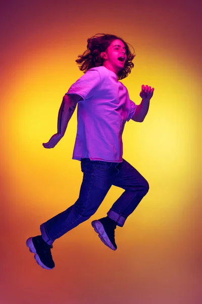 Full-length portrait of young excited man jumping isolated on orange background in neon light, filter. Concept of emotions, beauty, fashion — Stock Photo, Image