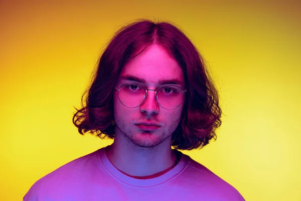 Porträt eines jungen Mannes, Student in legerer Kleidung, isoliert auf orangefarbenem Hintergrund in lila Neonlicht. Konzept von Emotionen, Schönheit, Mode — Stockfoto