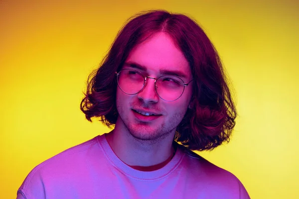 Retrato de jovem, estudante em roupas casuais isolado em fundo laranja em luz de néon roxo. Conceito de emoções, beleza, moda — Fotografia de Stock