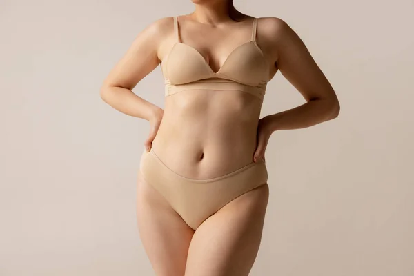 Retrato recortado de cuerpo femenino de aspecto natural en ropa interior beige posando aislado sobre fondo de estudio ligero — Foto de Stock
