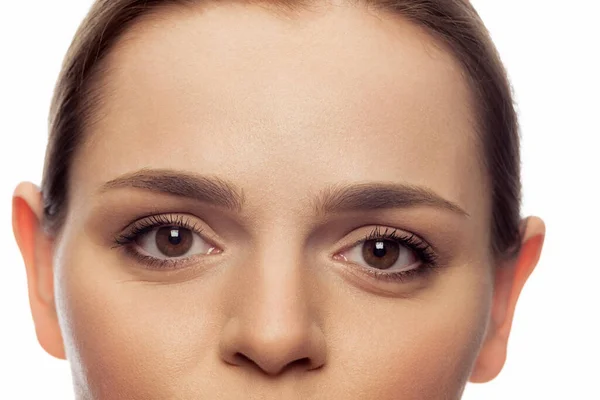 Imagem de close-up recortada de belos olhos castanhos femininos olhando para a câmera isolada sobre fundo estúdio branco — Fotografia de Stock