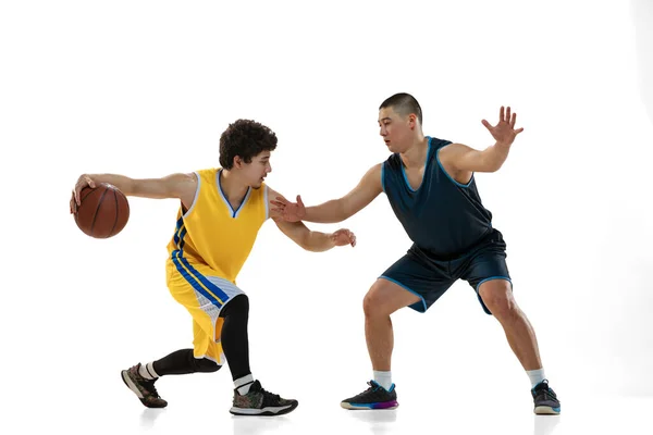 Dynamický portrét dvou mladých basketbalistů hrajících basketbal izolovaný na bílém pozadí studia. Pohyb, aktivita, sportovní pojmy. — Stock fotografie