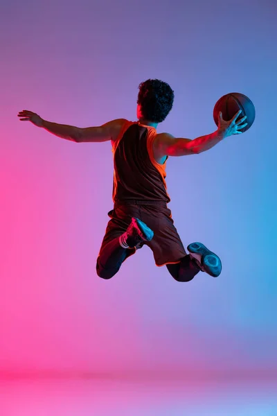 Junger, energiegeladener Mann beim Basketballspielen isoliert auf rosa-blauem Studiohintergrund im Neonlicht. Jugend, Hobby, Bewegung, Aktivität, Sportkonzepte. — Stockfoto