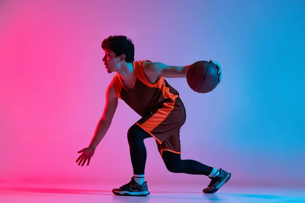 Спортивний чоловік грає в баскетбол ізольовано на градієнтному рожево-блакитному студійному фоні в неоновому світлі. Молодь, хобі, рух, діяльність, спортивні концепції . — стокове фото