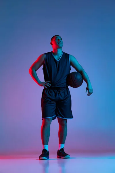 Retrato de comprimento total do jovem coreano com bola de basquete posando isolado no fundo do estúdio azul em luz de néon. Juventude, hobby, conceitos de esporte. — Fotografia de Stock