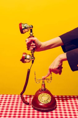 Retro objeler, pop sanat fotoğrafçılığı. Parlak sarı arka planda izole edilmiş klasik telefon ahizesini tutan kadın. Eski, eski tarz