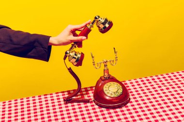 Retro objeler, pop sanat fotoğrafçılığı. Parlak sarı arka planda izole edilmiş klasik telefon ahizesini tutan kadın. Eski, eski tarz