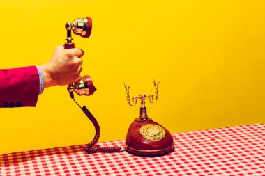Retro objeler, pop sanat fotoğrafçılığı. Parlak sarı arka planda izole edilmiş klasik telefon ahizesini tutan kadın. Eski, eski tarz