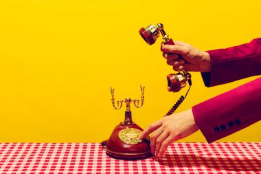 Retro objeler, pop sanat fotoğrafçılığı. Parlak sarı arka planda izole edilmiş klasik telefon ahizesini tutan kadın. Eski, eski tarz