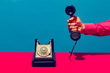 Retro nesneler, aletler. Mavi ve pembe arka planda izole edilmiş klasik telefon ahizesini tutan bir kadın. Klasik, eski moda tarzı. Pop sanat fotoğrafçılığı.