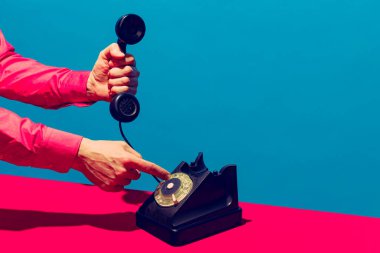 Retro nesneler, aletler. Mavi ve pembe arka planda izole edilmiş klasik telefon ahizesini tutan bir kadın. Klasik, eski moda tarzı. Pop sanat fotoğrafçılığı.