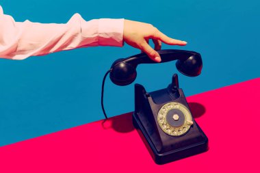 Retro nesneler, aletler. Mavi ve pembe arka planda izole edilmiş klasik telefon ahizesini tutan bir kadın. Klasik, eski moda tarzı. Pop sanat fotoğrafçılığı.