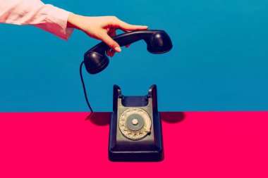 Retro nesneler, aletler. Mavi ve pembe arka planda izole edilmiş klasik telefon ahizesini tutan bir kadın. Klasik, eski moda tarzı. Pop sanat fotoğrafçılığı.