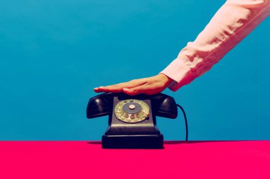 Retro nesneler, aletler. Mavi ve pembe arka planda izole edilmiş klasik telefon ahizesini tutan bir kadın. Klasik, eski moda tarzı. Pop sanat fotoğrafçılığı.