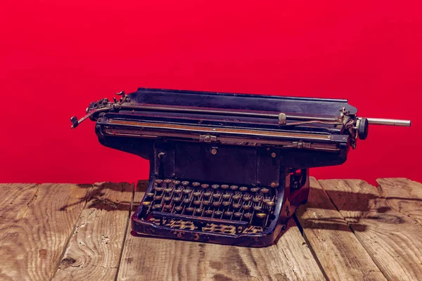 Pop art photography. Retro old, shabby typewriter standing on wooden table isolated on bright red background. Vintage, retro style. — Stock Photo, Image