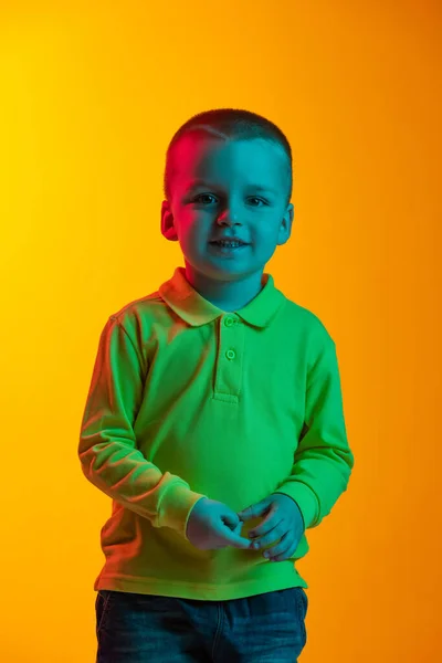 Portret van een schattig jongetje, geïsoleerd lachend op een gele studio backgroud in neon licht. Concept van kinderemoties, gezichtsuitdrukking, kindertijd — Stockfoto