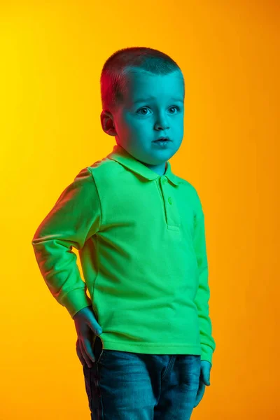 Portret van een verbaasd jongetje geïsoleerd op een gele studio in neonlicht. Concept van kinderemoties, gezichtsuitdrukking, kindertijd — Stockfoto