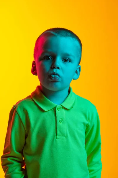 Portrait of cute little boy making face isolated on yellow studio backgroud in neon light. Concept of child emotions, facial expression, childhood — Stock Photo, Image