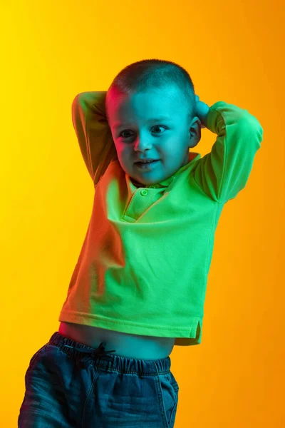 Portret van een schattig jongetje, geïsoleerd lachend op een gele studio backgroud in neon licht. Concept van kinderemoties, gezichtsuitdrukking, kindertijd — Stockfoto