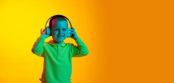 Gelukkige schattige kleine jongen, kind glimlachend geïsoleerd op gele studio backgroud in neon licht. Concept van kinderemoties, gezichtsuitdrukking, kindertijd — Stockfoto