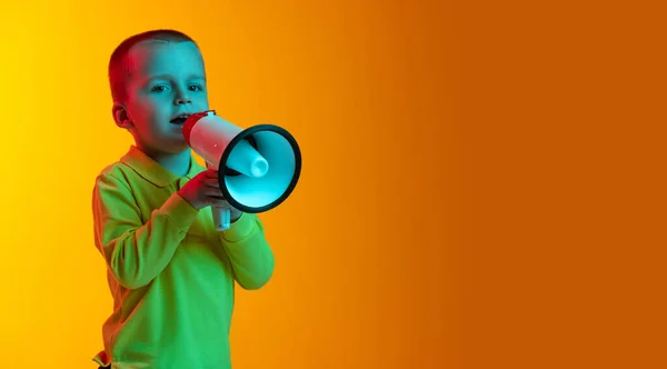 Um menino em roupas de estilo casual segurando megafone isolado em backgroud estúdio amarelo em luz de néon. Conceito de emoções infantis, expressão facial, infância — Fotografia de Stock