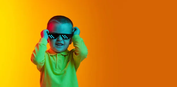 Gelukkige schattige kleine jongen, kind glimlachend geïsoleerd op gele studio backgroud in neon licht. Concept van kinderemoties, gezichtsuitdrukking, kindertijd — Stockfoto