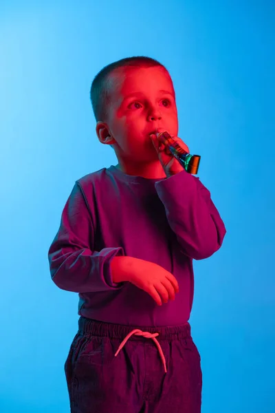 Portrait de petit garçon, enfant, enfant d'âge préscolaire isolé sur fond bleu studio en néon rouge. Concept d'émotions de l'enfant, expression faciale, enfance — Photo