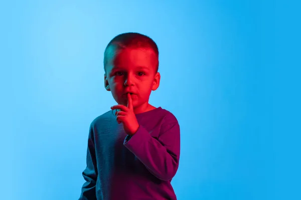 小さな男の子、子供、就学前の年齢の子供の肖像画は、赤いネオンの光の中で青いスタジオの背景に隔離されています。子供の感情、表情、子供時代の概念 — ストック写真