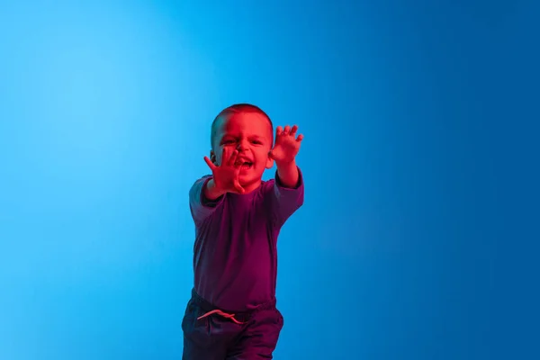 Portrait of little crying boy, kid, preschool age child is capricious isolated on blue studio backgroud in red neon light. Concept of child emotions, facial expression, childhood — Stock Photo, Image
