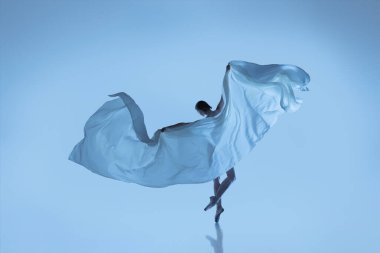 Esnek kadın portresi, kumaşla dans eden zarif balerin mavi stüdyo arka planında izole edilmiş kumaş. Zarafet, sanat, güzellik konsepti. Ağırlıksız, şefkatli..